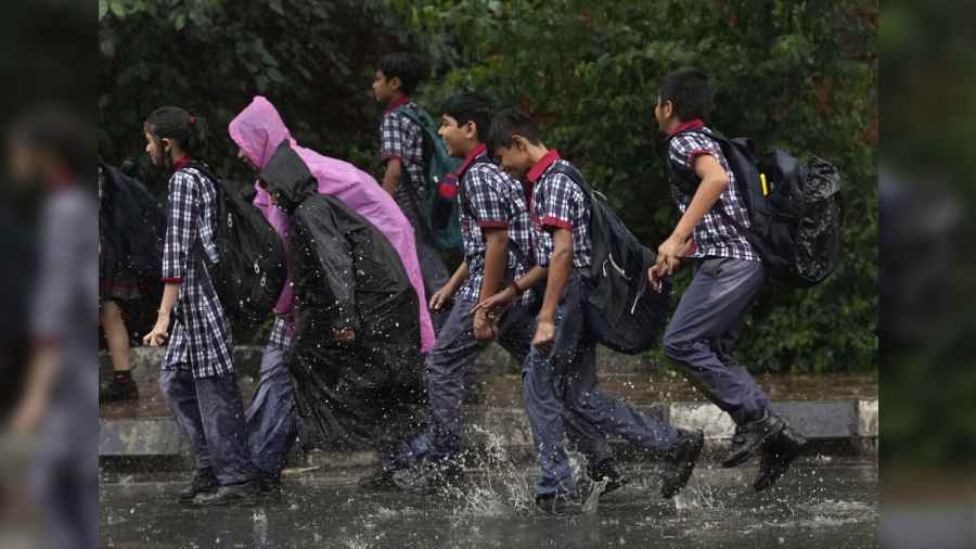 School students walk through a waterlogged road during rain, in New Delhi