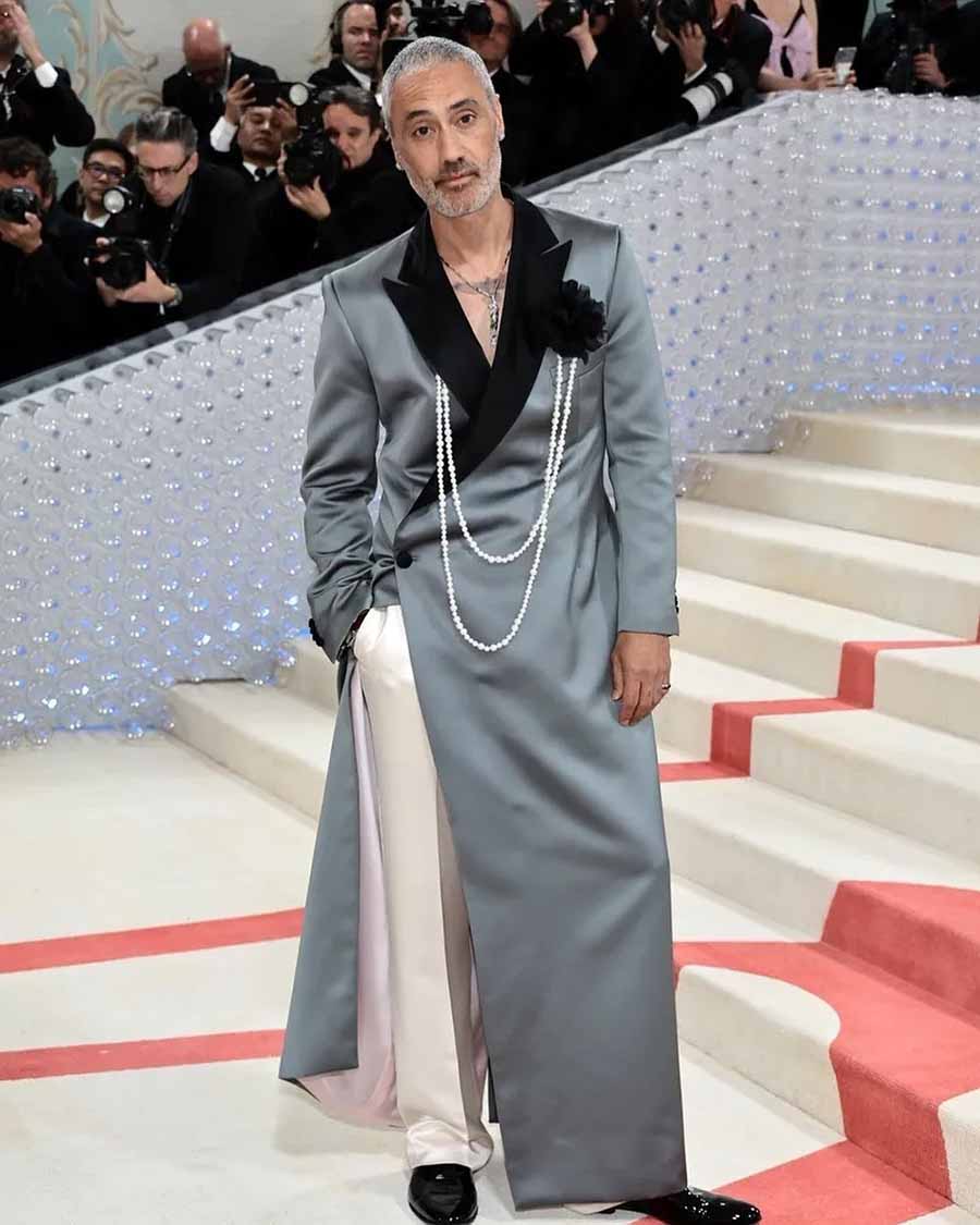Filmmaker Taika Waititi⁠ wore a Prabal Gurung floor-length structured coat with white satin trousers and pearl chains. ⁠