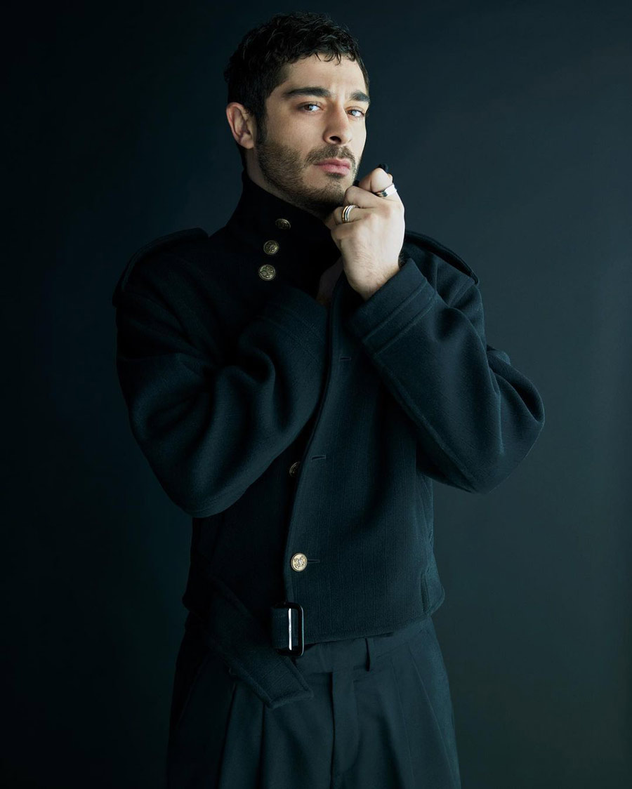 In an all-black formal outfit with gold buttons, Deniz poses for a picture.