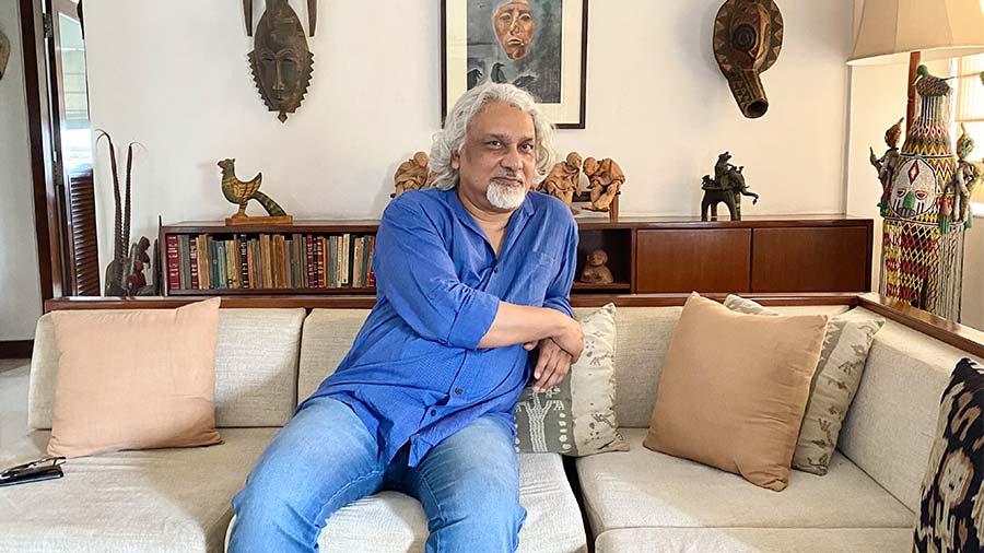 Author Kunal Basu at his residence in south Kolkata. On the wall behind him is a gouache artwork done by the author himself