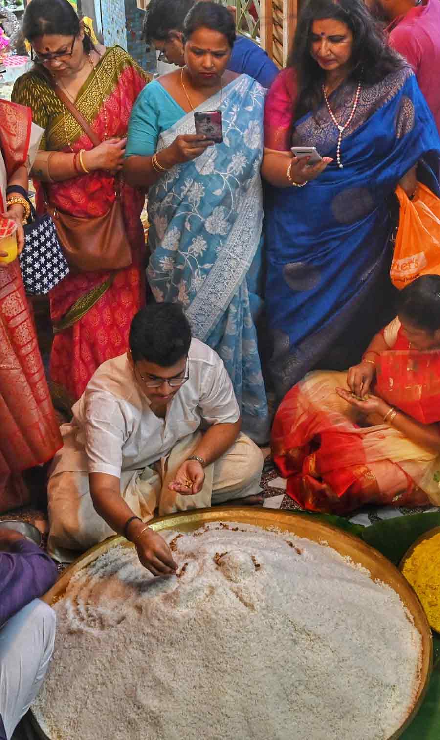 Women takes snapshots of the main ‘prasad’ being mixed by a priest at the Bagbazar house