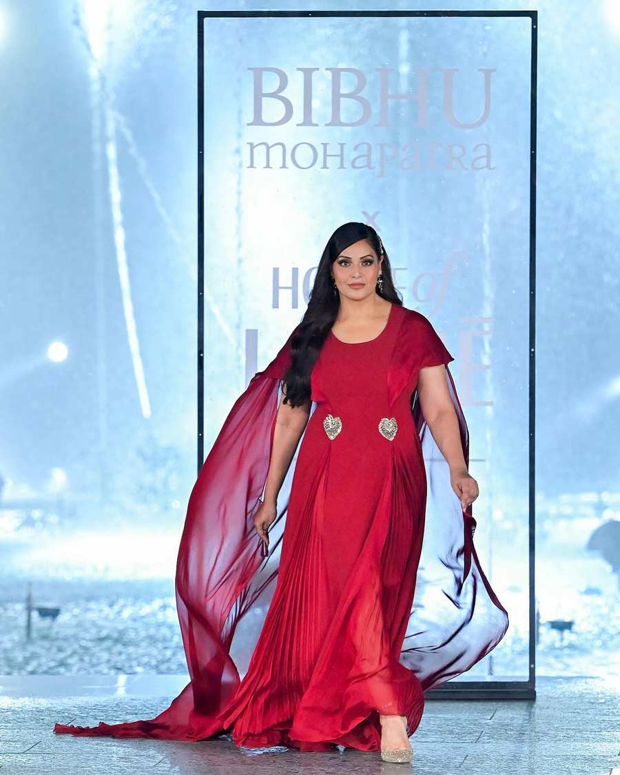 Bipasha Basu walked the ramp in a deep red gown with a round neck, glittery silver heart-shaped patterns on the waist and a pleated skirt designed by Bibhu Mohapatra. She also wore a netted cape-like sweep train at the back.