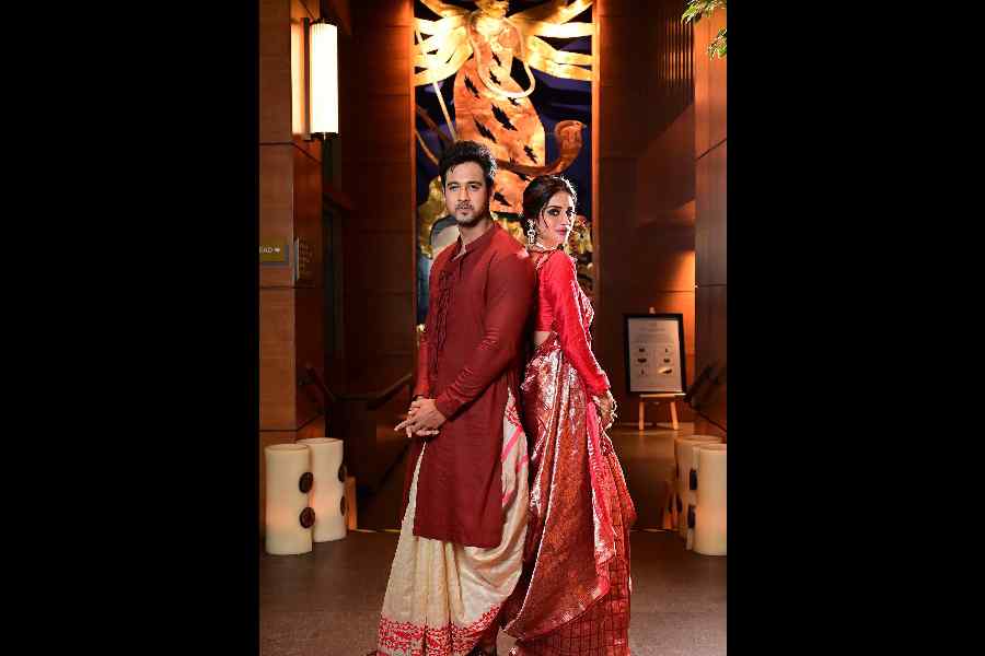Yash and Nussrat look absolutely gorgeous in traditional and rich hues. The imposing work of art at Taj City Centre New Town forms the perfect backdrop. Yash's Gram of Ink kurta and Parama dhoti match Nussrat's beautiful Soumitra Mondal red jacquard sari. Rohan Arora's footwear completes Yash's Bangali babu look. Nussrat wears pieces by Crisanto Jewels, smokey kohl eyes, nude lips, a messy low bun and flowers that we picked from her bouquet! #jugaad