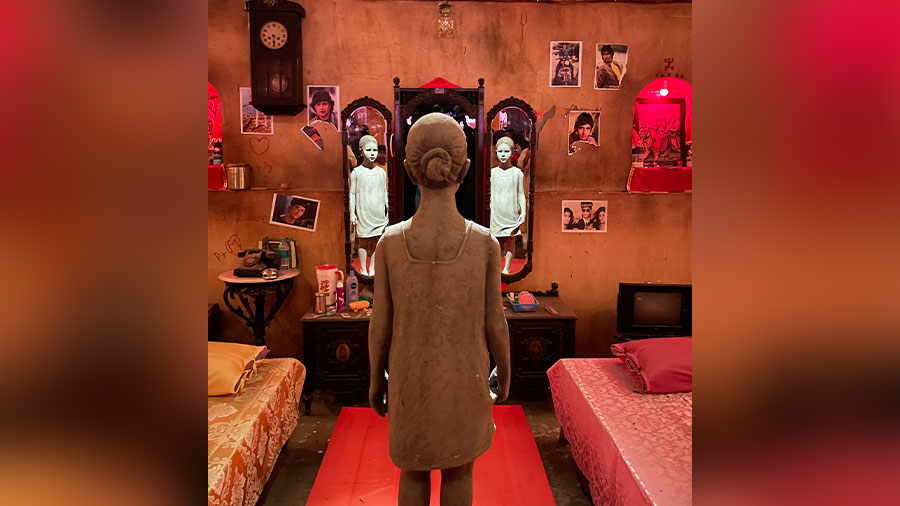 A life-size statue of a girl looking into a three-part mirror as part of the installation