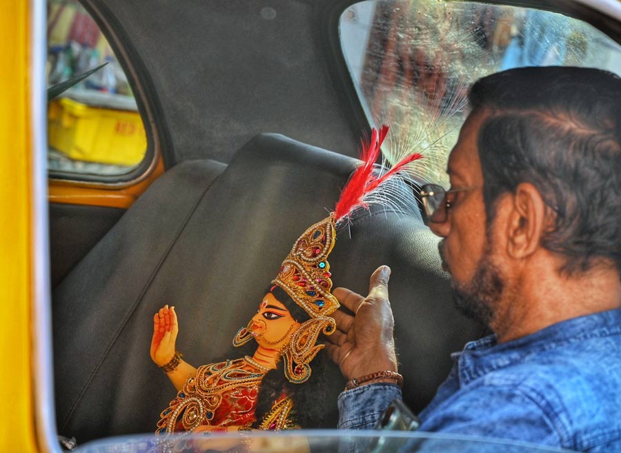 An elderly man takes an idol of Lakshmi in a yellow taxi