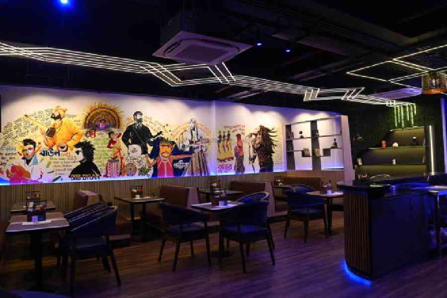 Graffiti consisting of figures from world folk music designed by Snita and painted by Basit Hossain adorn the walls of the space that has blue lights and neutral-toned furniture.