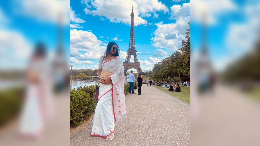 Suchanda in traditional white sari with red border in front of the Eiffel Tower