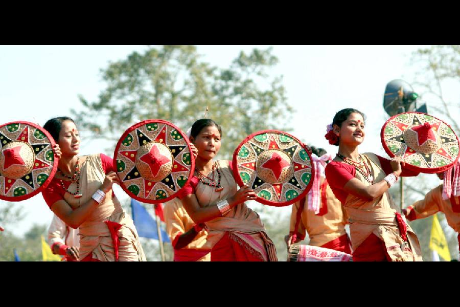 Assamese women holding jaapis perform the Bihu dance.