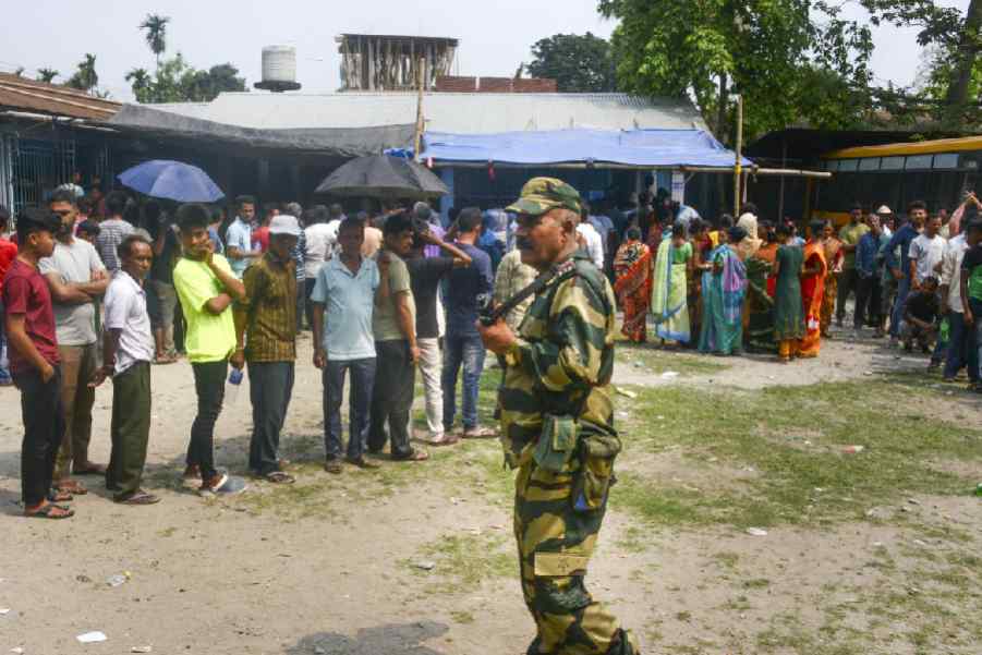 A security personnel stands guard as voters wait in a queue at a polling station to cast their votes for the first phase of Lok Sabha elections in Jalpaiguri.