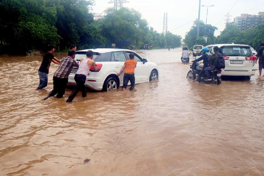 People push a car stuck on a waterlogged road after heavy monsoon rain, in Gurugram
