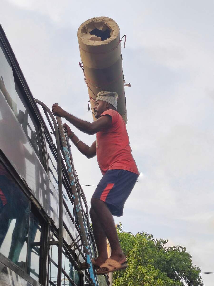 A labourer lifts heavy goods on the roof of a long-distance bus at Esplanade