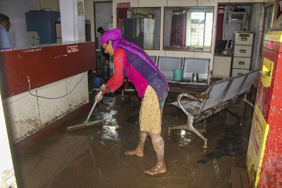 A woman cleans after water entered inside a bank following rains, near Dehradun, Friday, Aug. 23, 2024.