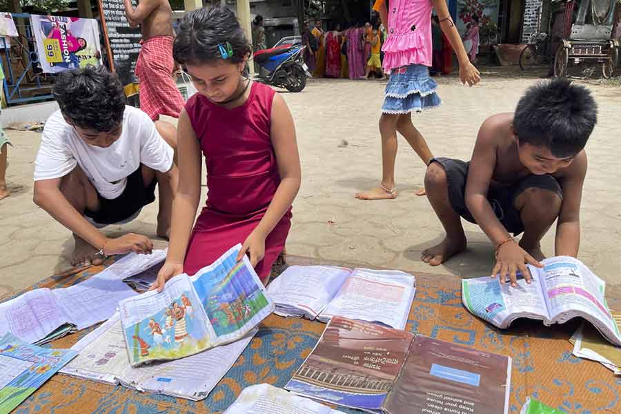 Flood-affected children check their textbooks that were kept to dry under the sun at a relief shelter, in Agartala, Saturday, Aug. 24, 2024.
