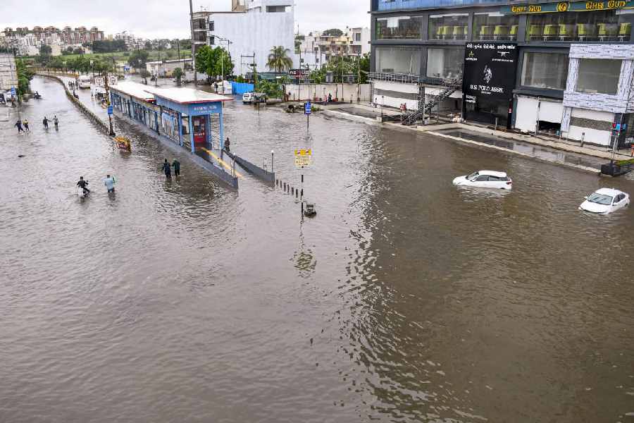 People pass through waterlogged road after heavy rains, in Rajkot, Tuesday, Aug. 27, 2024.