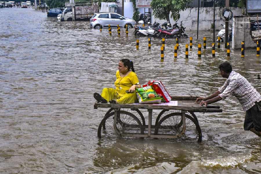 A labourer pushes a cart carrying a woman to help her cross a flooded road after heavy monsoon rainfall, in Vadodara, Tuesday, Aug. 27, 2024. 