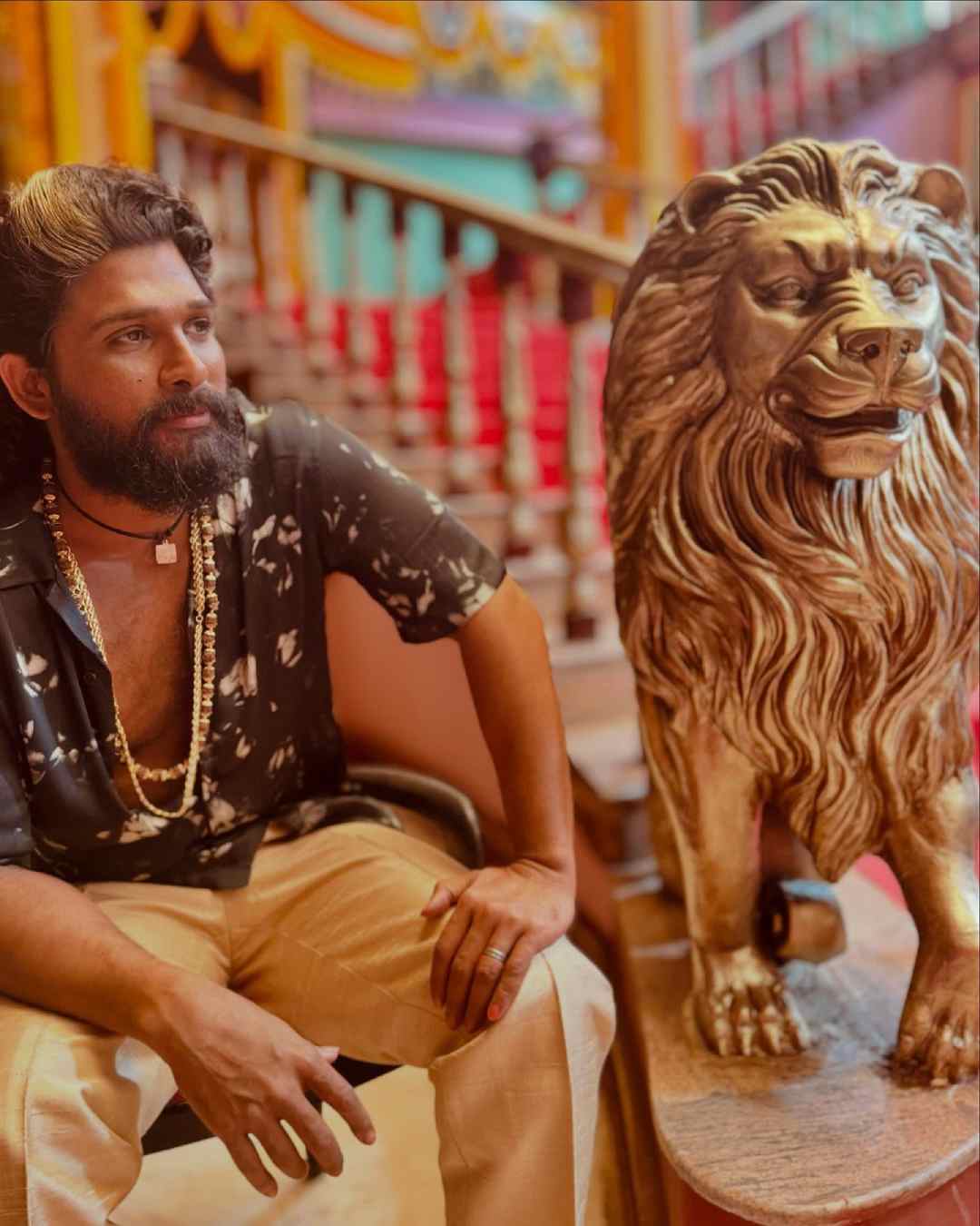 A picture shows Allu sporting a black printed shirt paired with beige pants, and posing next to a statue of a lion, reflecting the boldness of his character Pushpa Raj in the film. 