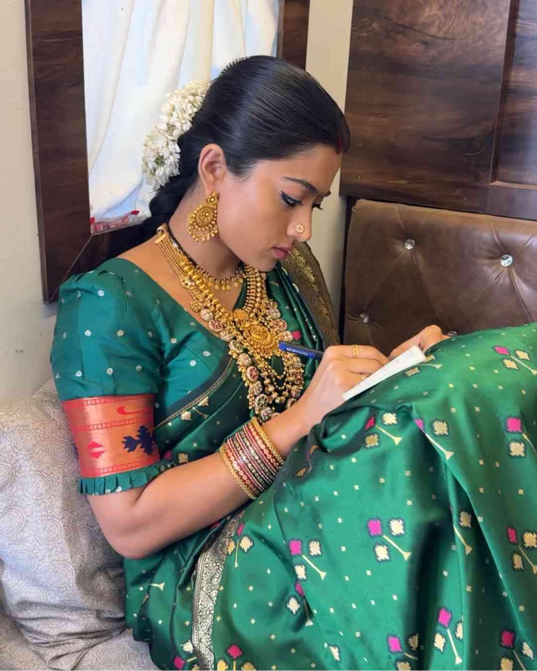Rashmika was engrossed in scribbling in her notebook in one of the photos. She looked radiant in a green sari, which she accesorised with a golden necklace, danglers, bangles and a nath. A gajra and a red bindi completed her look. 
