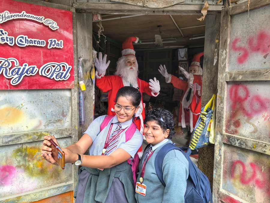 Two schoolgirls pose with a Santa Claus made by potter Raja Pal at Kumartuli 