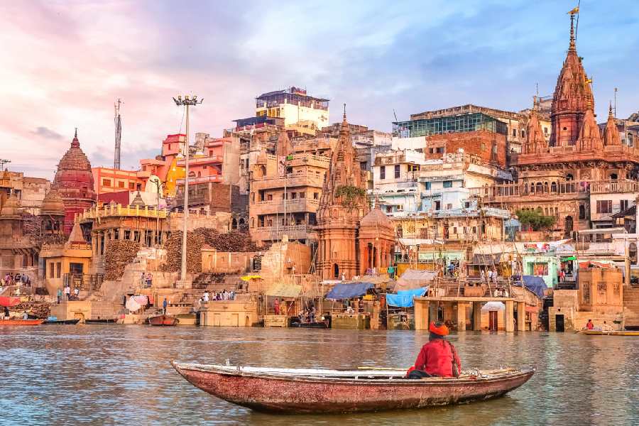 Hindu sadhu sitting on a boat overlooking Varanasi city architecture at sunset