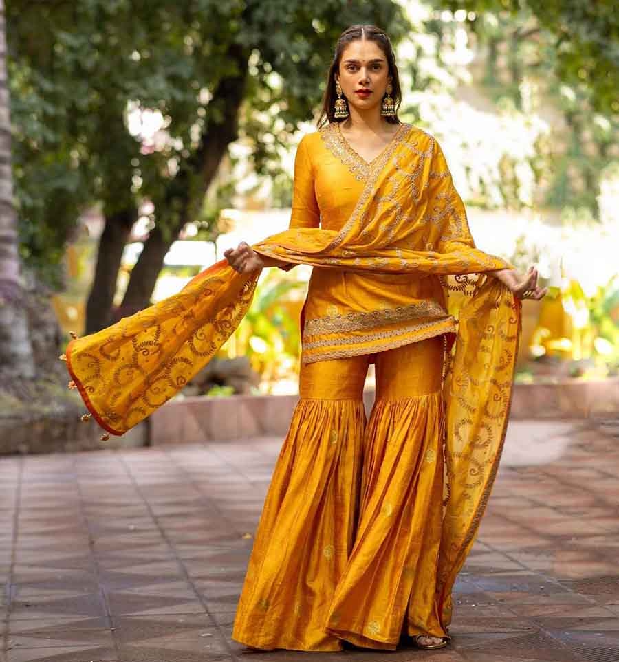 Aditi Rao Hydari looks resplendent in a yellow Mughal Gharara set by Punit Balana. Middle-parted open hair, nude makeup, red lips and a black bindi completed the look.