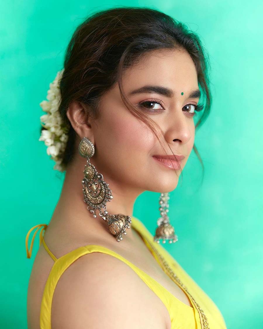 A yellow sari with a sleeveless blouse, a gajra, three-layered jhumkas and a green bindi are a great combo for Saraswati Puja.