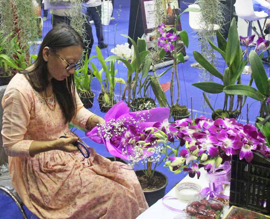 A woman focuses on crafting a bouquet with orchids