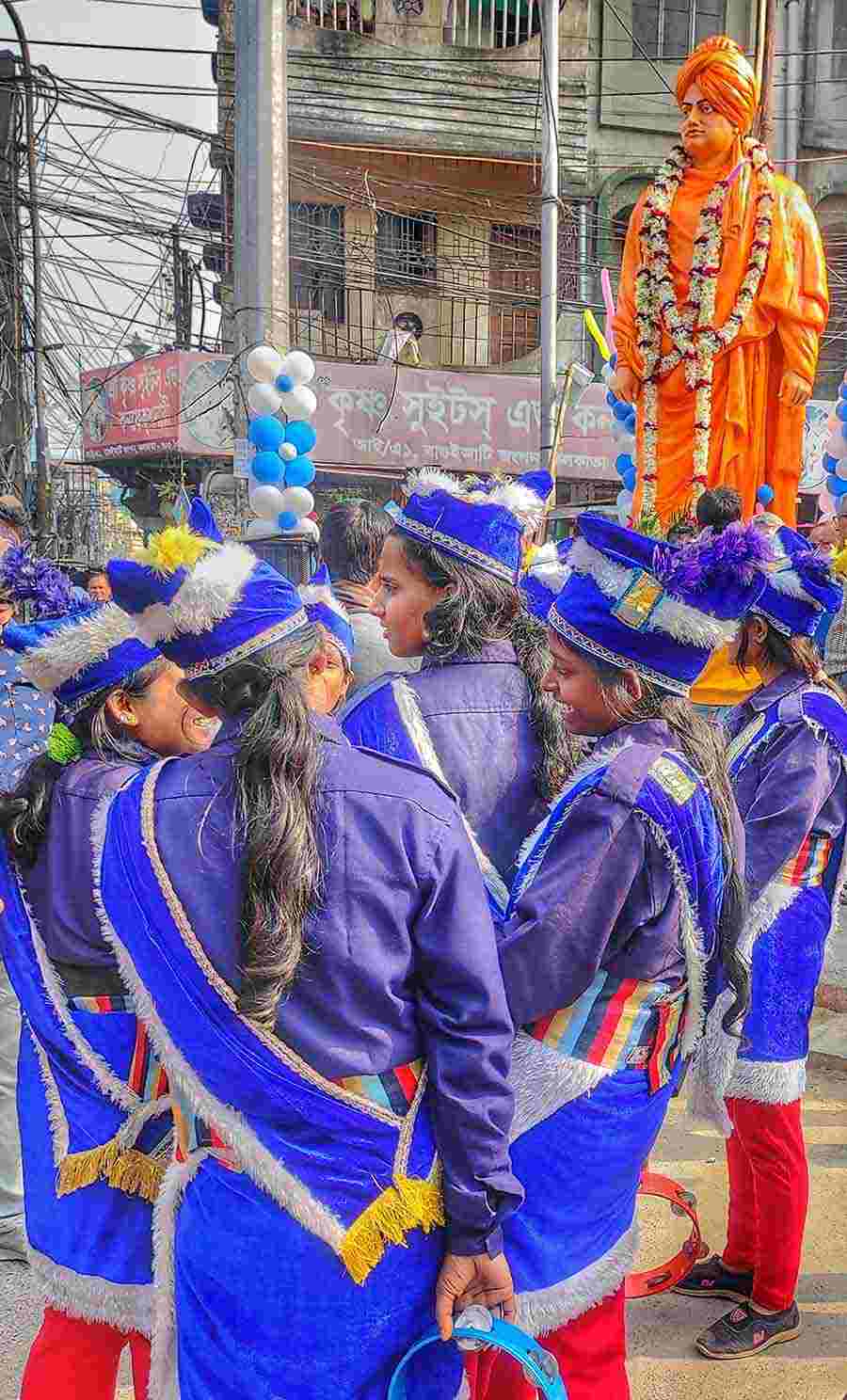Girls of a musical band huddle together in front of a statue of Swami Vivekananda