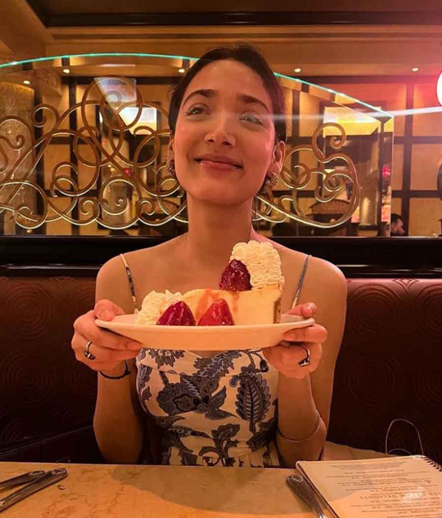 A happy girl with a plate full of strawberry cheesecake with extra cream.