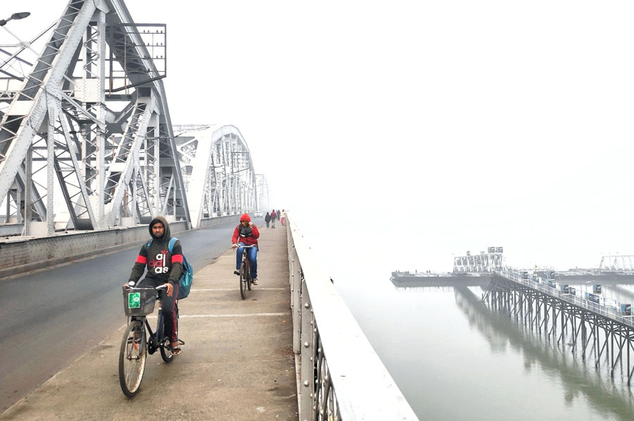 Cyclists pass fog-enveloped Bally bridge and Dakshineswar Ghat on Saturday morning