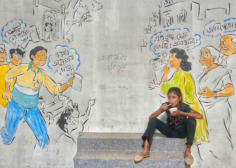 A youngster relishes a snack in front of a wall adorned with graffiti in Bagbazar