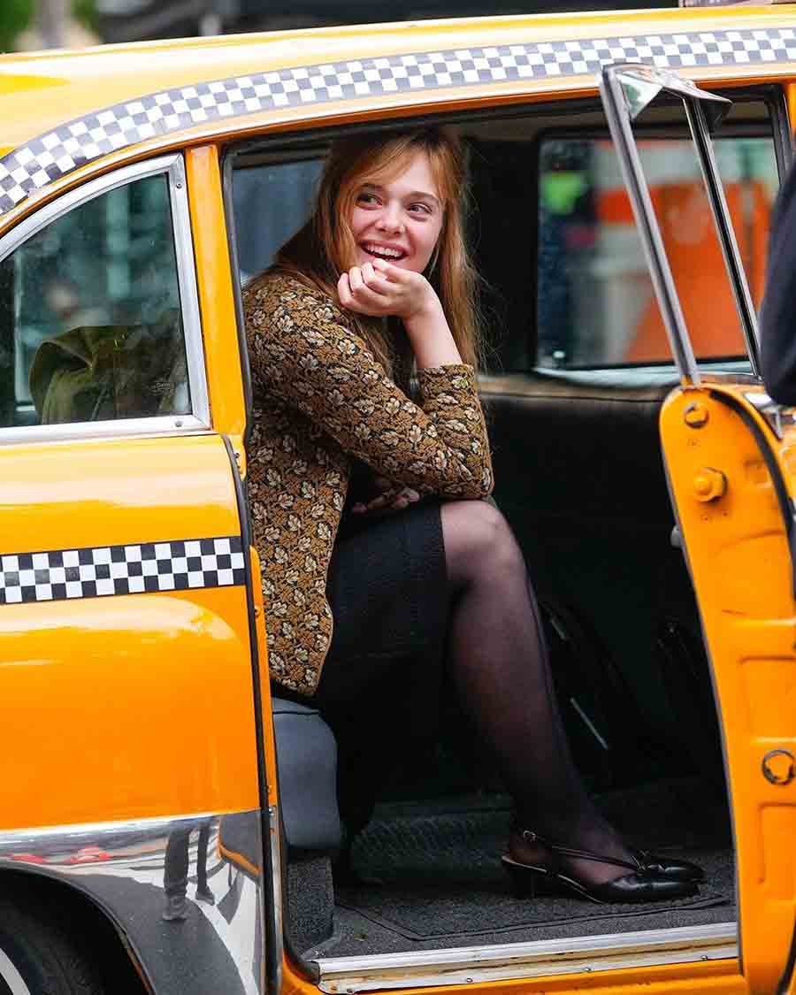 For a shot in New Jersey, Fanning sported a floral knit sweater paired with a shimmery black mini-skirt and net stockings. She smiled at people outside while sitting inside a taxi.