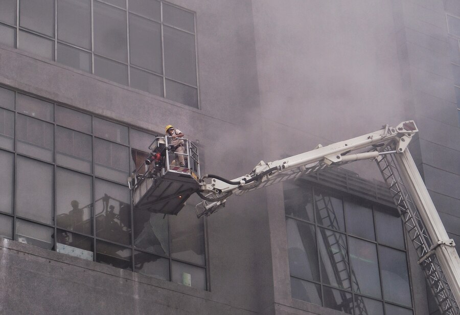 Firemen atop a hydraulic ladder smash the glass sheets to let the smoke out