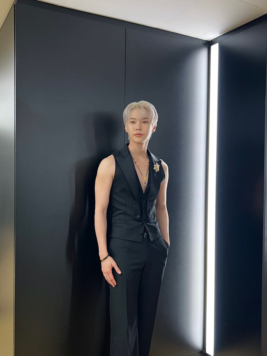 NCT’s Doyoung opted for a chic all-black look for the Dolce & Gabbana Spring Summer 2025 men’s show. A sleeveless vest, black rosary necklace, and a golden floral brooch comprised his ensemble.