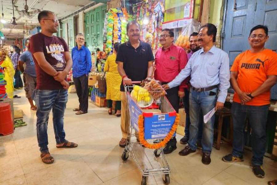 A customer carries his shopping in a trolley at CA Market as local councillor Rajesh Chirimar looks on