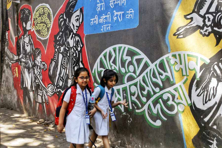Two schoolgirls walk past a wall adorned with graffiti on their way back home on International Women’s Day at Beckbagan on Friday
