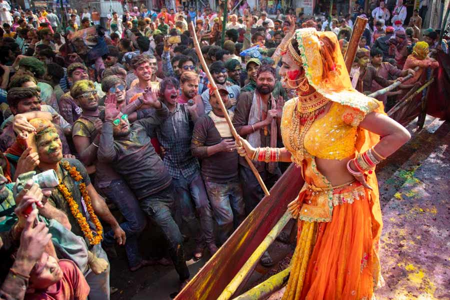A woman playfully threatens revellers with a stick (lathi) during Lathmar Holi celebrations 