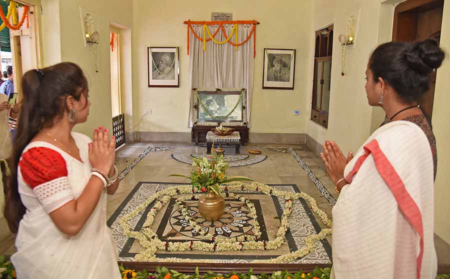 Two young women fold their hands to garlanded photographs of Tagore at Thakurbari