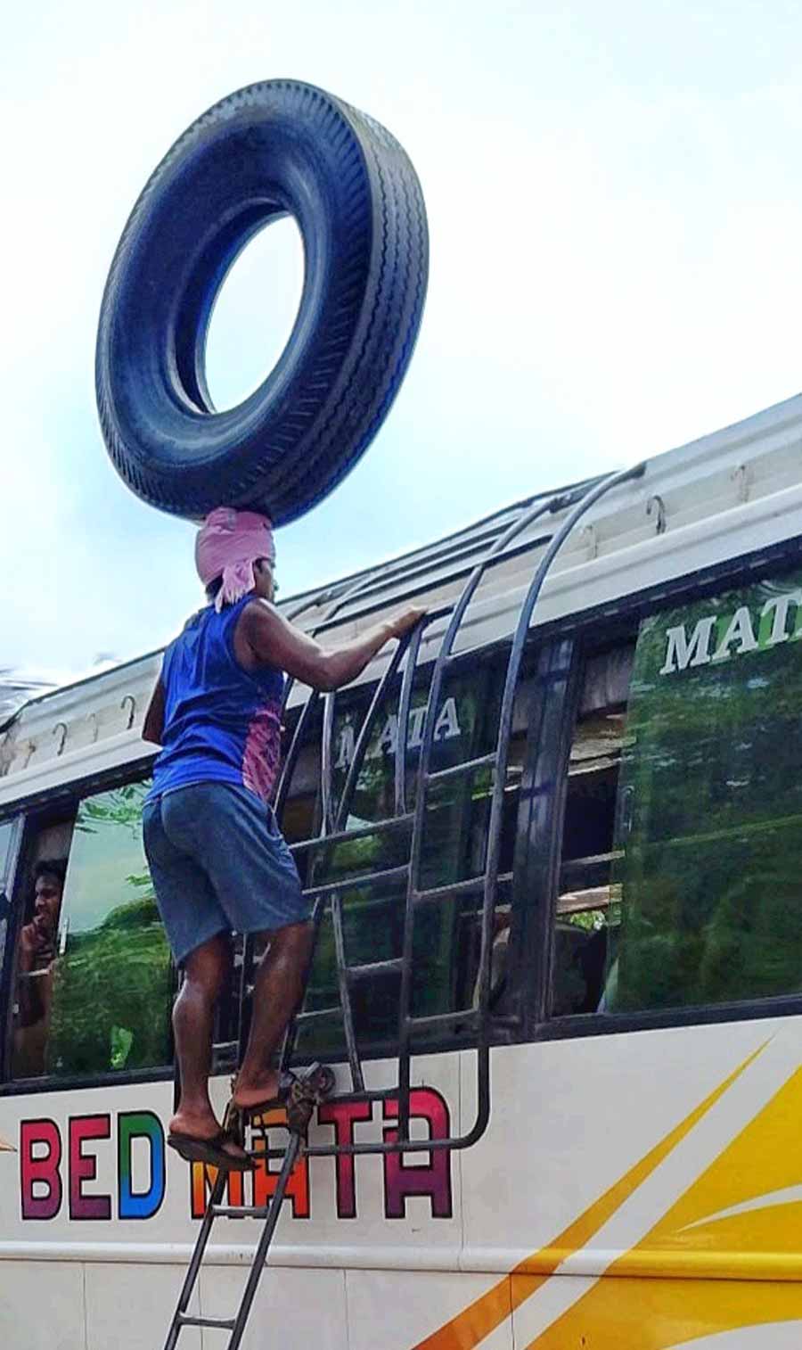 A labourer balances a heavy-duty tyre on his head as he climbs a ladder to reach the roof of a bus 