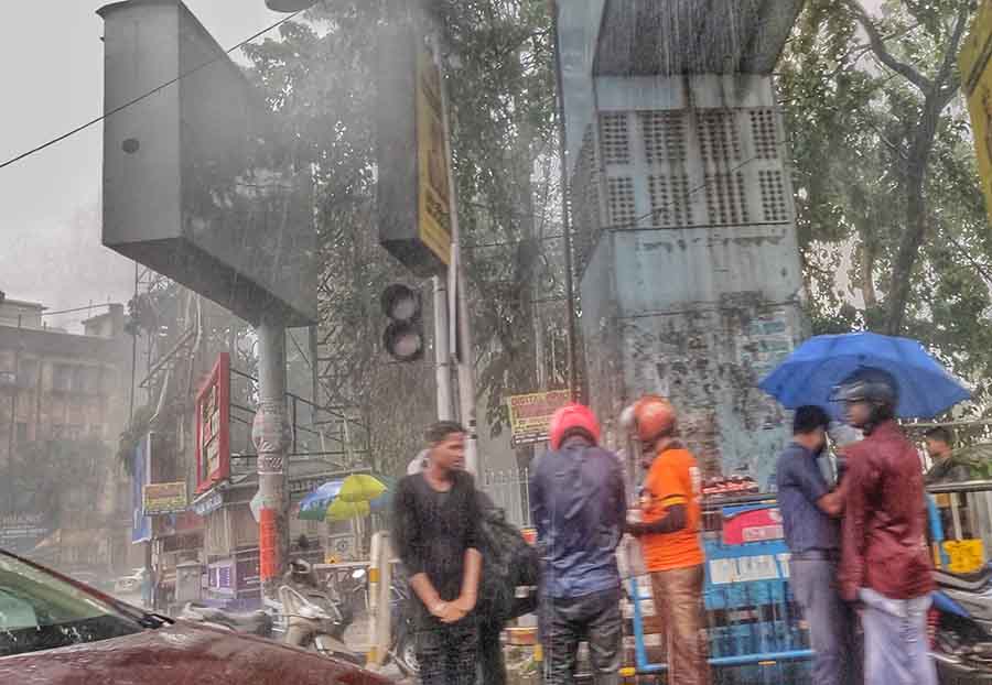Motorcyclists and other pedestrians huddle together under a shade at a street crossing