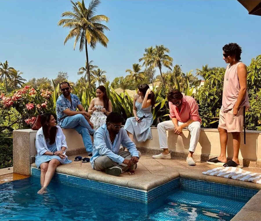 Kartik lounged by a swimming pool in a pink shirt paired with white pants, matching sneakers and trendy sunglasses. 