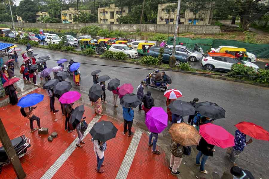 People holding umbrellas stand along a road amid rains due to ‘Spawn’ cyclone.
