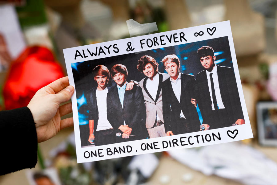 A person holds a poster with an image of One Direction band members as fans gather and place tributes to former One Direction singer Liam Payne in the Tuilleries Garden, Paris, France, October 20, 2024.