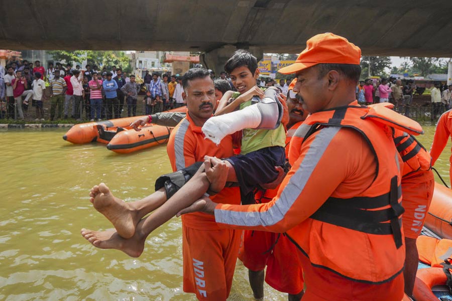 NDRF personnel carry a boy with a plaster cast on his arm as they conduct rescue operations after floodwater entered the Kendriya Vihar apartment following heavy rain, in Bengaluru.