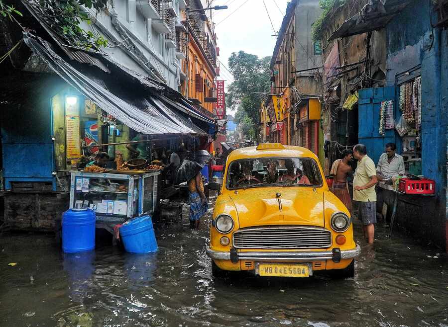 A yellow taxi negotiates a narrow waterlogged lane in Bowbazar through the tea stalls 