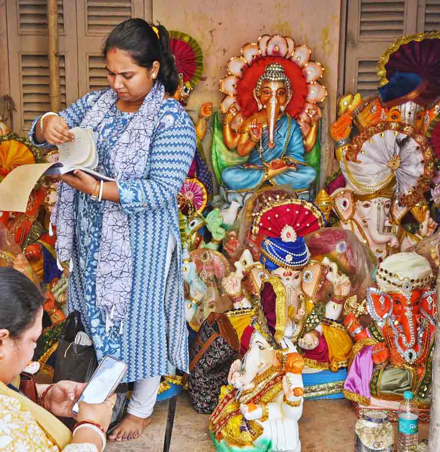 An artist searches the bill book for an order on Ganesh idols while customers wait at Kumartuli