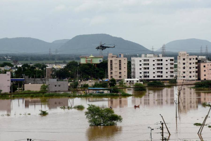 People row small boats in a flooded neighbourhood as a chopper carrying relief material flies, following heavy rains in Vijayawada on September 2, 2024