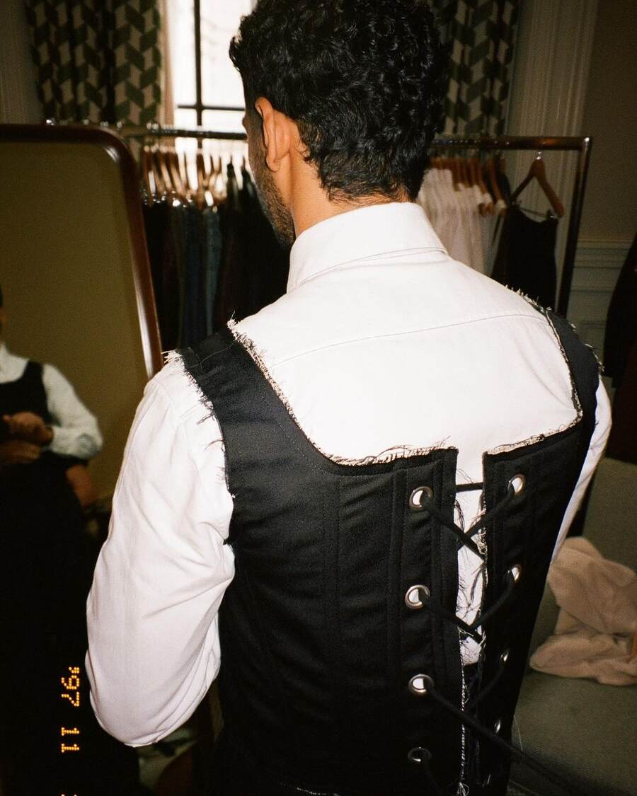 Ishaan dons a three-piece suit featuring a double-breasted jacket over a crisp white shirt. He also opts for a black corset instead of a vest for his character and a sleek white tie. 