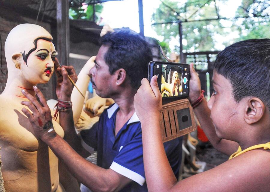A boy captures his artisan father drawing the eyes of a Vishwakarma idol ahead of the puja on September 17