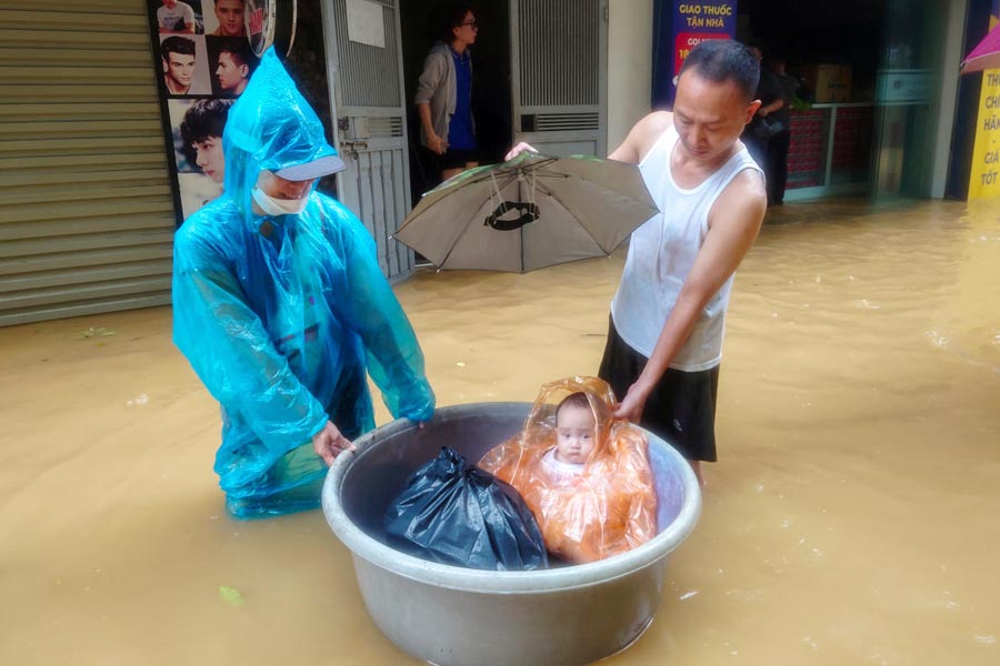 A boy sits in a floating basket as people wade through a flooded street following the impact of Typhoon Yagi, in Hanoi, Vietnam, September 11, 2024 