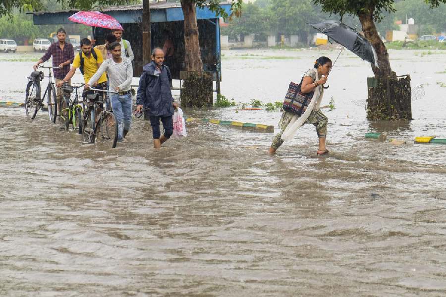 Commuters wade through a waterlogged road during heavy rains, in Gurugram.